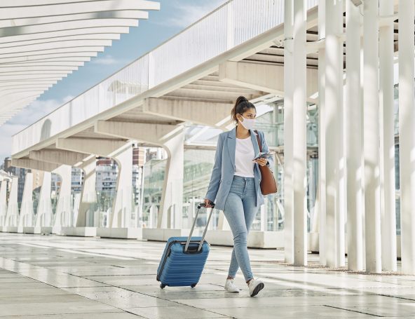 Mulher andando em aeroporto arrastando uma mala e usando máscara